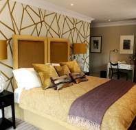 A bedroom with a double bed, white and yellow table lamps on the sides and white walls with golden lines