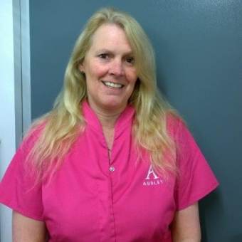 A smiling blond lady in a pink care uniform