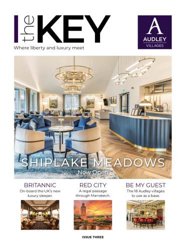 Read the next edition of The Key magazine A modern, elegant lounge area with blue chairs, gold accents, and a bar counter, featured on the cover of "The Key" magazine for Audley Villages' Shiplake Meadows opening.