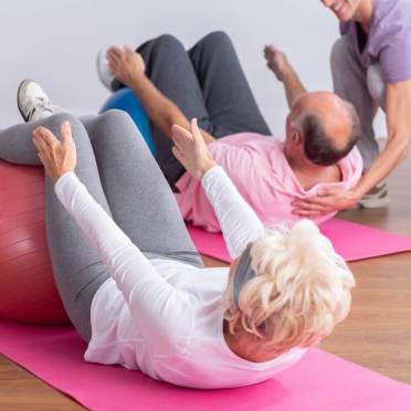 A senior woman and man on mats, face up, legs on gym ball in a crunch