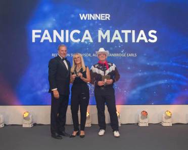 Three people stand on a stage with blue lighting; a woman holds a plaque. The screen reads "Winner Fanica Matias.