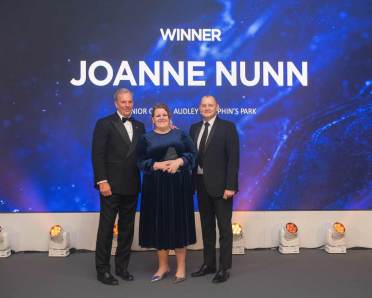 Three people standing on stage under a "Winner Joanne Nunn" sign at an award ceremony.