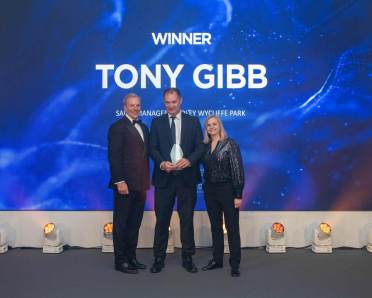 Three people stand on stage, one holding an award. The screen behind them reads "Winner Tony Gibb.