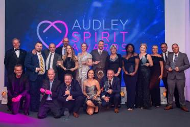 A group of people posing on stage holding awards in front of a sign reading "Audley Spirit Awards.