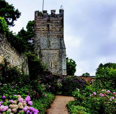 A stone tower stands amidst a garden with colorful hydrangeas under a cloudy sky.