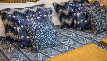 A bed with a blue patterned bedspread and multiple blue patterned throw pillows.