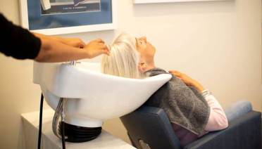 A person is reclining in a salon chair with their hair being washed in a basin by a stylist.