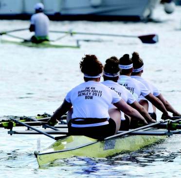 Four rowers in matching outfits compete in a rowing event, gliding through the water in a yellow boat.