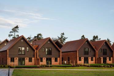 Row of modern, two-story brick houses with triangular roofs and large windows, set against a clear sky backdrop.