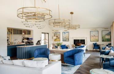 Modern lounge area with blue and white furniture, circular chandeliers, art on walls, and a bar with a coffee machine.