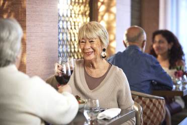 Two older adults enjoying drinks and conversation at a restaurant, with another couple seated in the background.