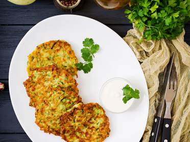Courgette blini on a white plate served with sour cream and parsley on top
