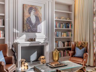 Library at St Elphin's Park Elegant living room with two armchairs, a fireplace, and built-in bookshelves. A painting hangs above the fireplace, and a chess set is on a glass coffee table in the center.