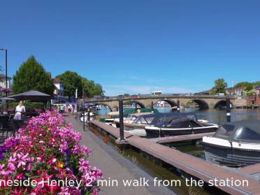 Henley-on-Thames A riverside walkway in Henley with boats docked, colorful flowers in the foreground, and a stone bridge in the background; text reads "Thameside Henley 2 min walk from the station.